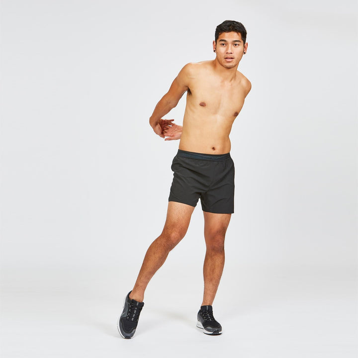 Full body shot of male model stretching in Janji 5" AFO Middle Shorts