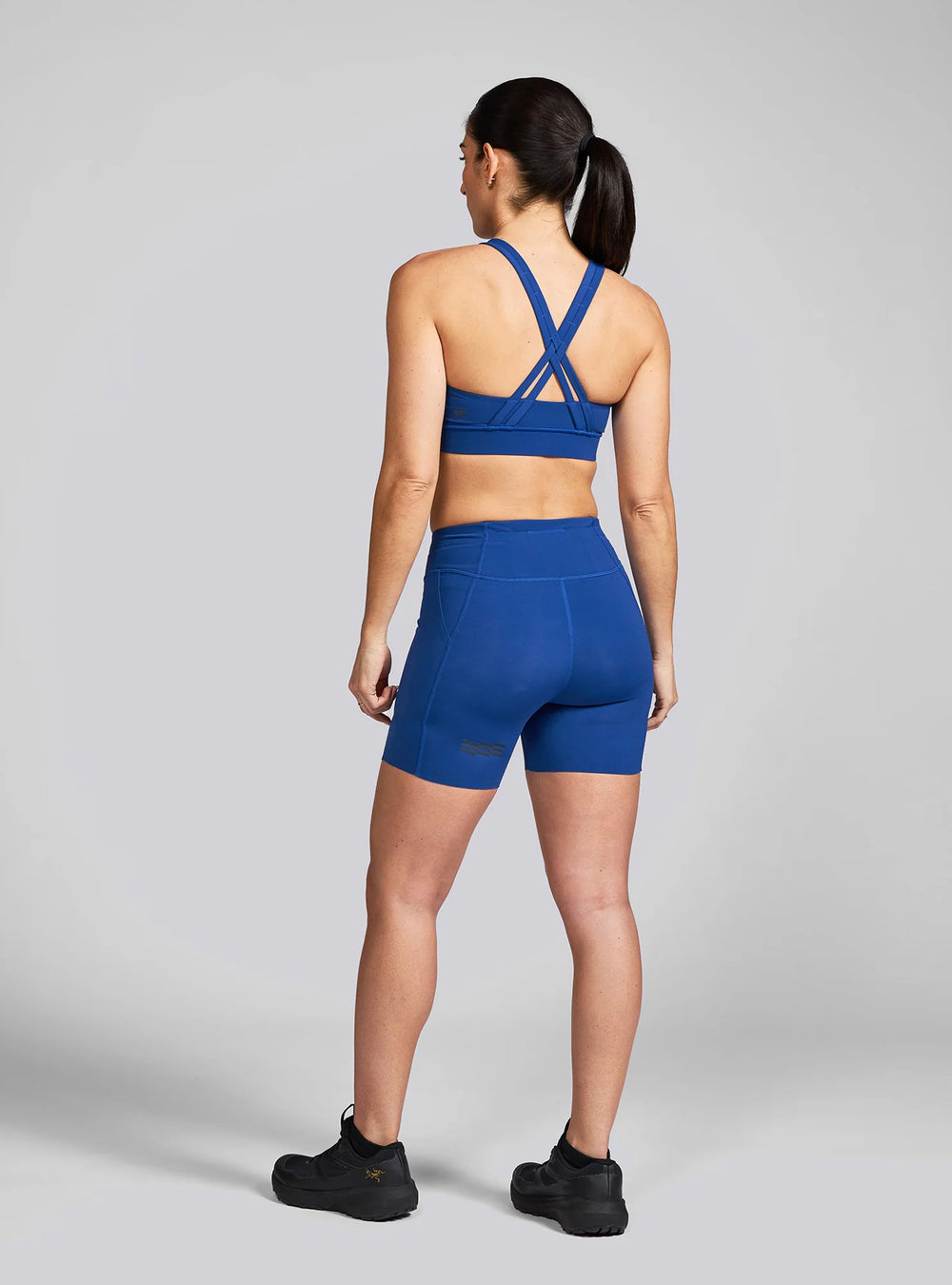 ull back view of Janji Women’s 5" Pace Shorts worn by female runner, showcasing reflective details and ergonomic waistband.